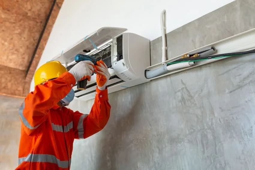 Instalador con mono naranja y casco atornillando un split en una pared de hormigón de Málaga, con la canaleta y los tubos al lado