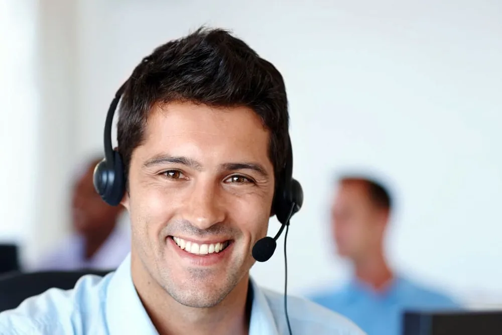 Persona de atención al cliente con auriculares y micrófono que sonríe ante un ordenador, imagen de la coordinación de avisos de electrodomésticos en Elche
