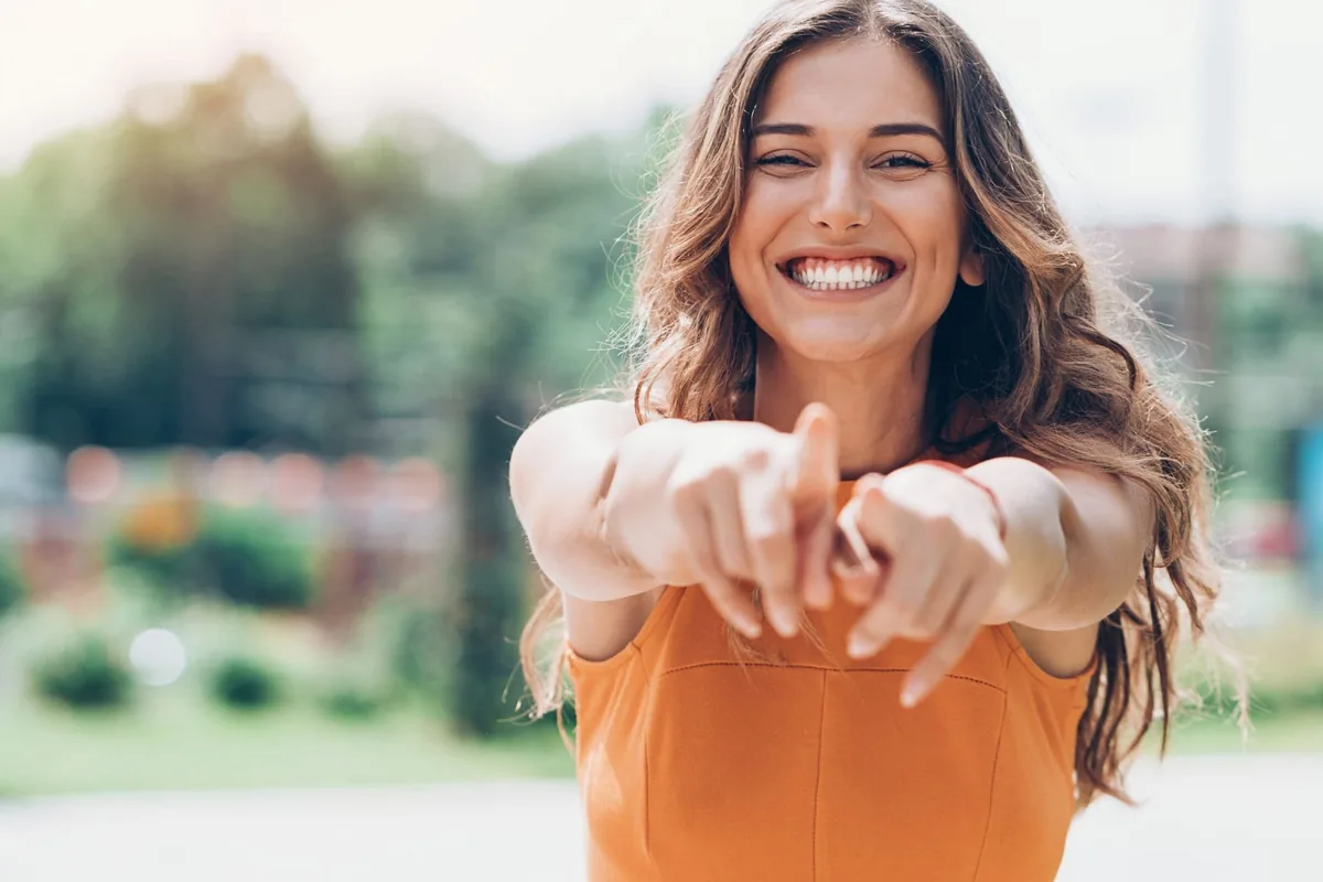 Mujer sonriente con vestido naranja que señala a cámara en un parque, imagen de la atención al cliente en los avisos de electrodomésticos de A Coruña