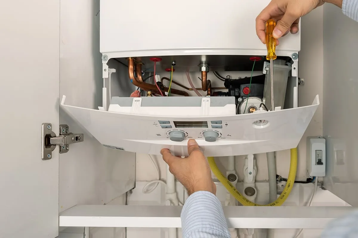Manos abatiendo con un destornillador el frontal de un calentador de gas instalado dentro de un mueble de cocina en Barcelona
