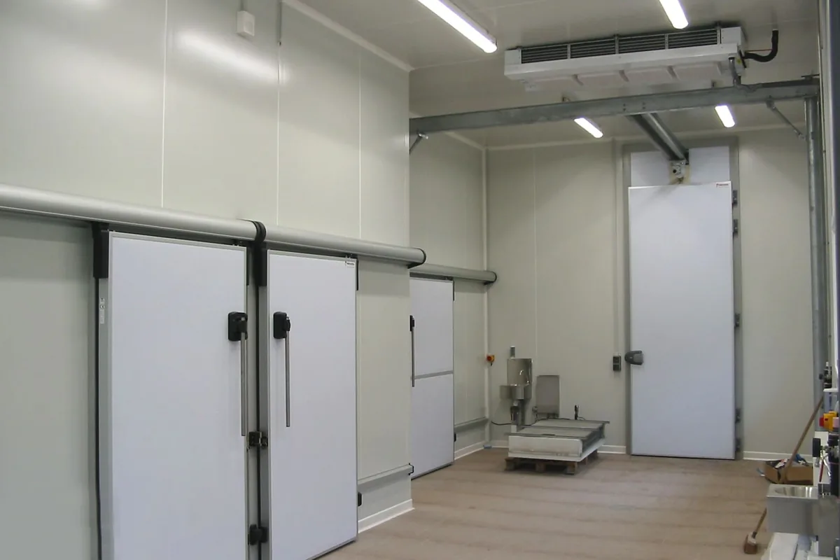 Sala de un obrador de Sevilla con tres puertas correderas de cámara frigorífica en fila, evaporador industrial en el techo y puerta de congelación al fondo