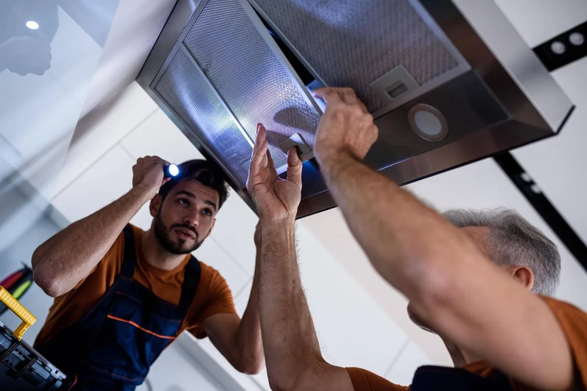 Dos técnicos inspeccionan con linterna los filtros de una campana decorativa de acero en un piso de Madrid