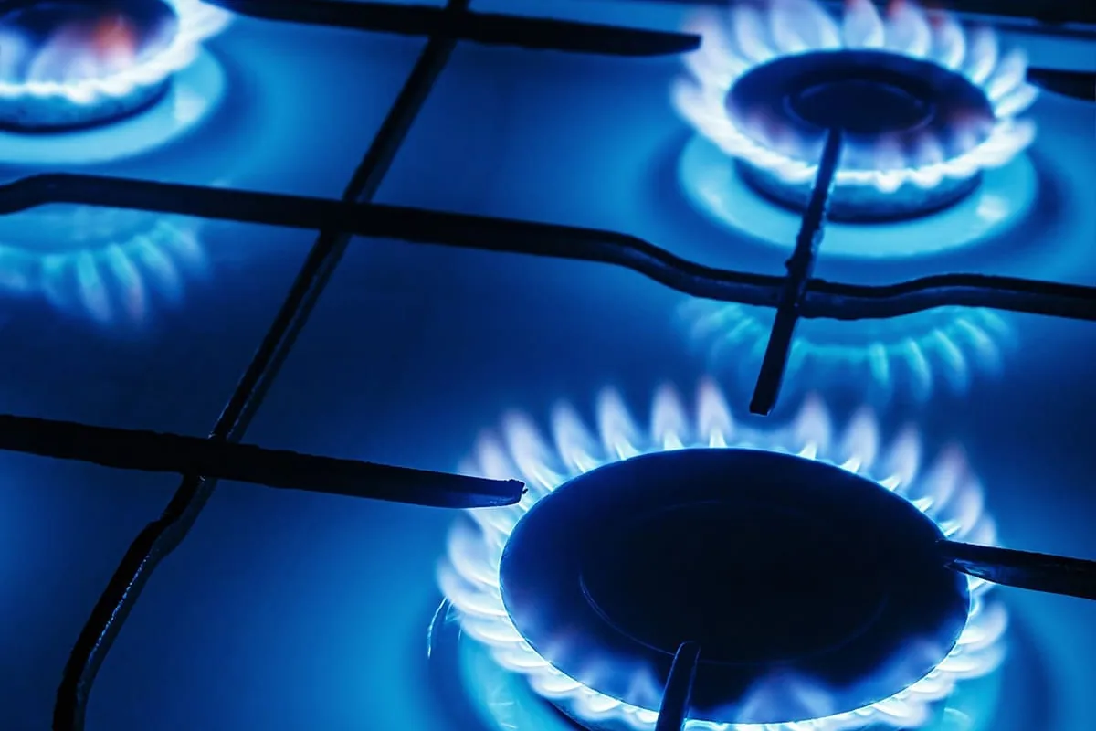 Tres quemadores de una cocina de gas encendidos en penumbra, con coronas de llama azul sobre parrillas negras, en una vivienda de Córdoba
