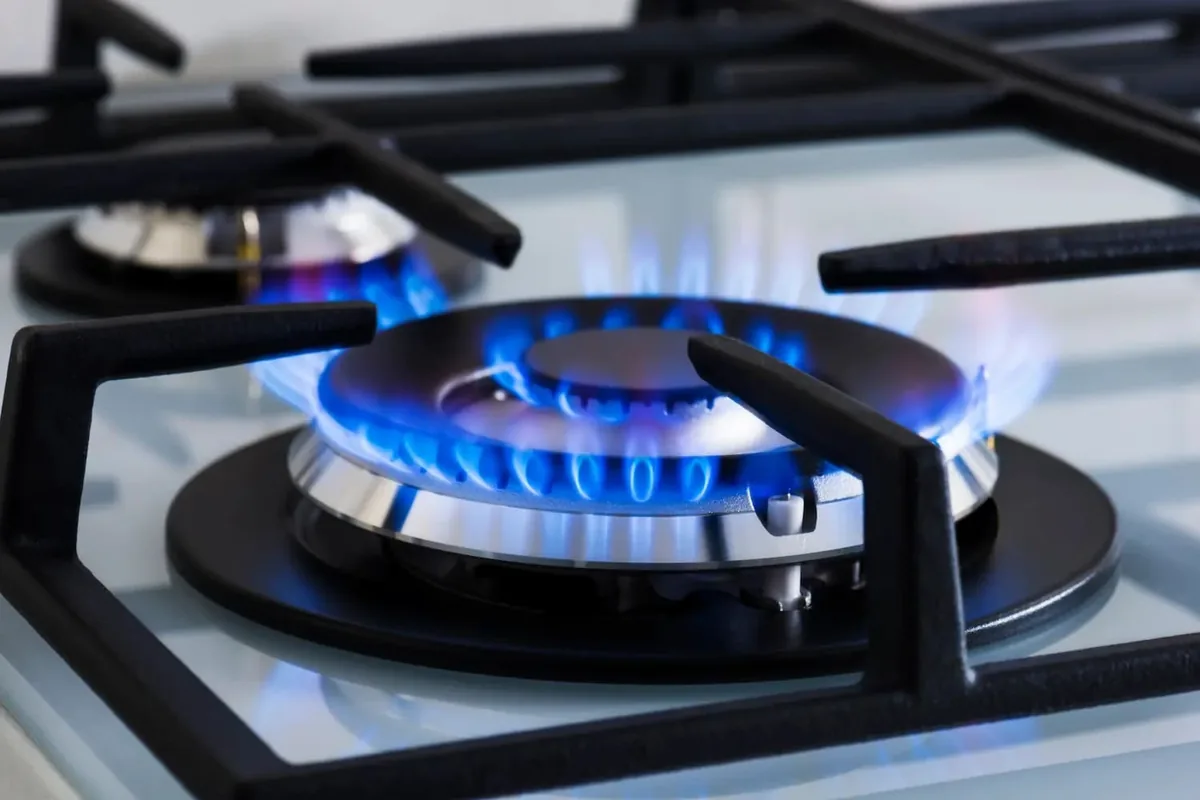 Quemador de gas encendido con llama azul regular sobre una encimera blanca y parrillas de fundición negras en una vivienda de Málaga