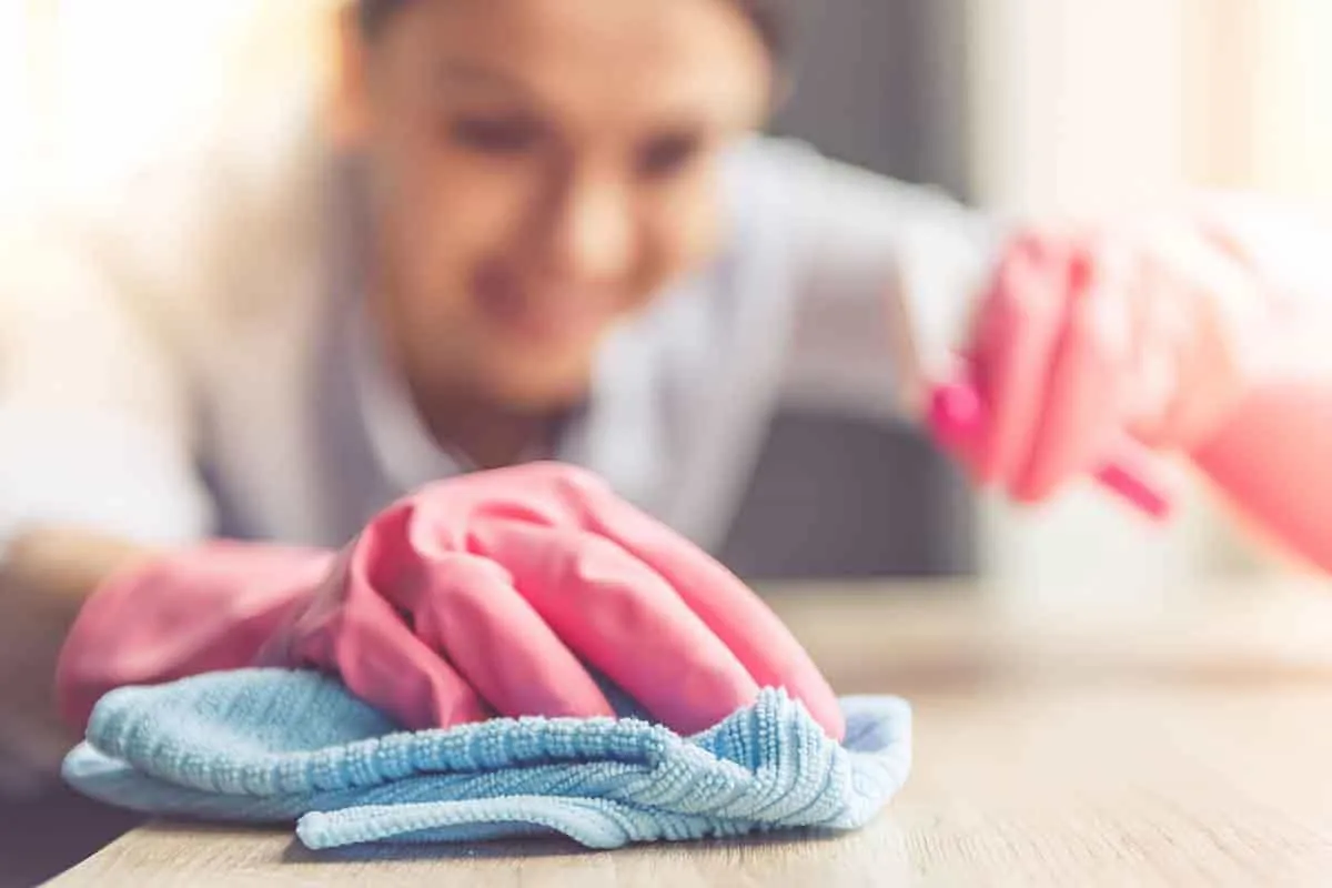 Manos con guantes rosas y un paño de microfibra azul que recorren un mostrador de madera clara en un comercio de Elche