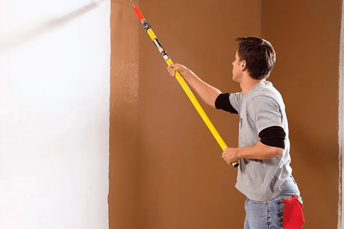 Pintor en Sevilla pasando un rodillo con alargador sobre una pared blanca que va cubriendo de color tierra