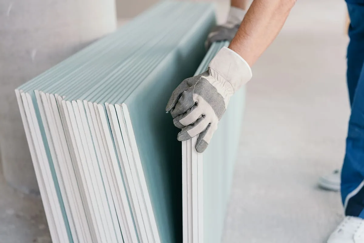 Operario con guantes separa una placa de yeso laminado de una pila apoyada en la pared, preparada para levantar tabiques en una reforma de Zaragoza