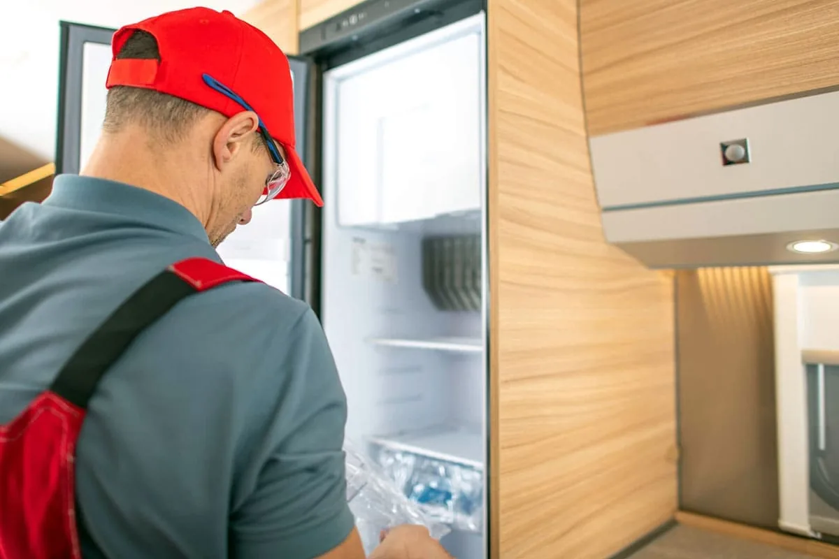 Técnico con gorra roja y mono de trabajo que se asoma al interior de un frigorífico integrado abierto, con las baldas y el cajón a la vista, en una cocina de Granada