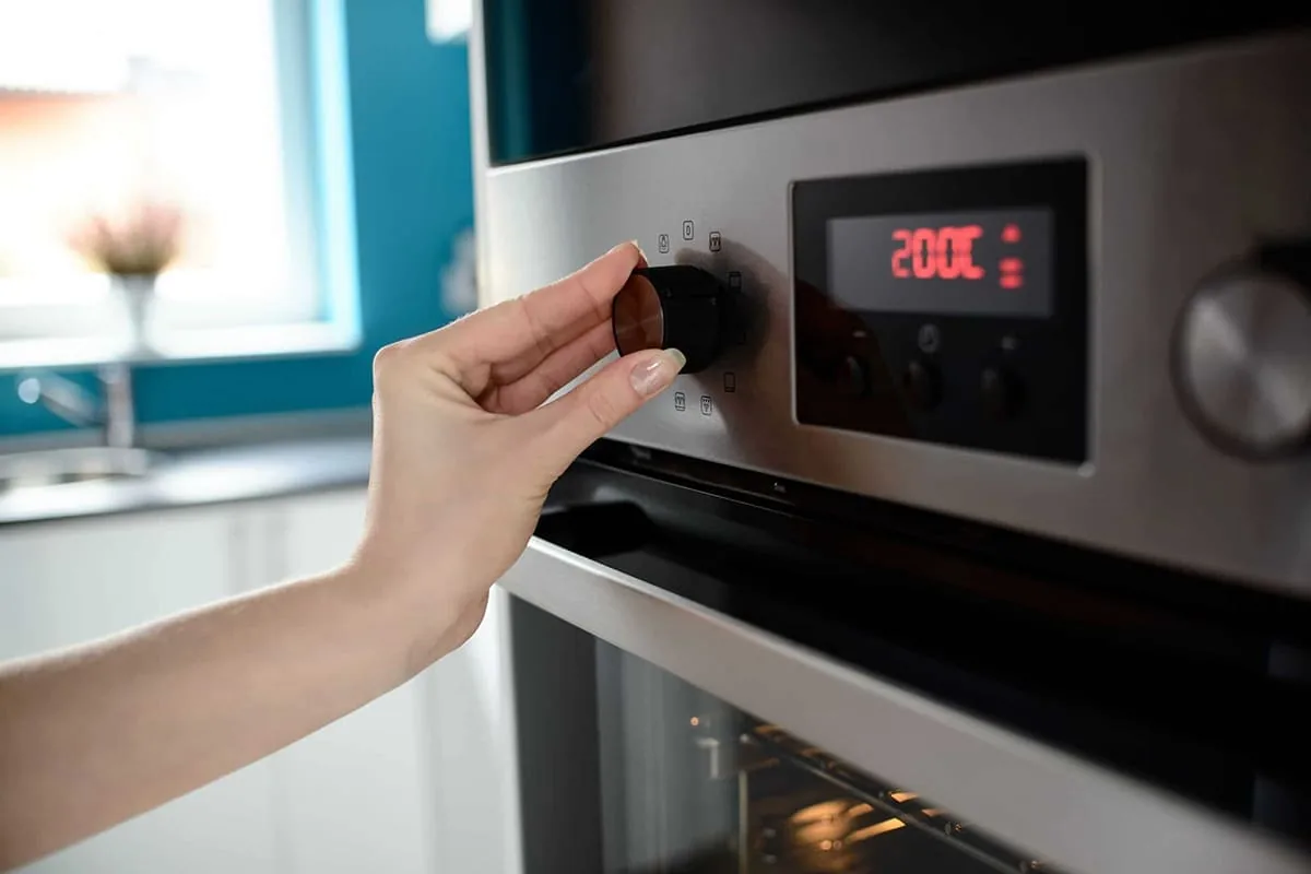 Mano girando el selector de funciones de un horno eléctrico con pantalla digital encendida en una cocina de Valencia