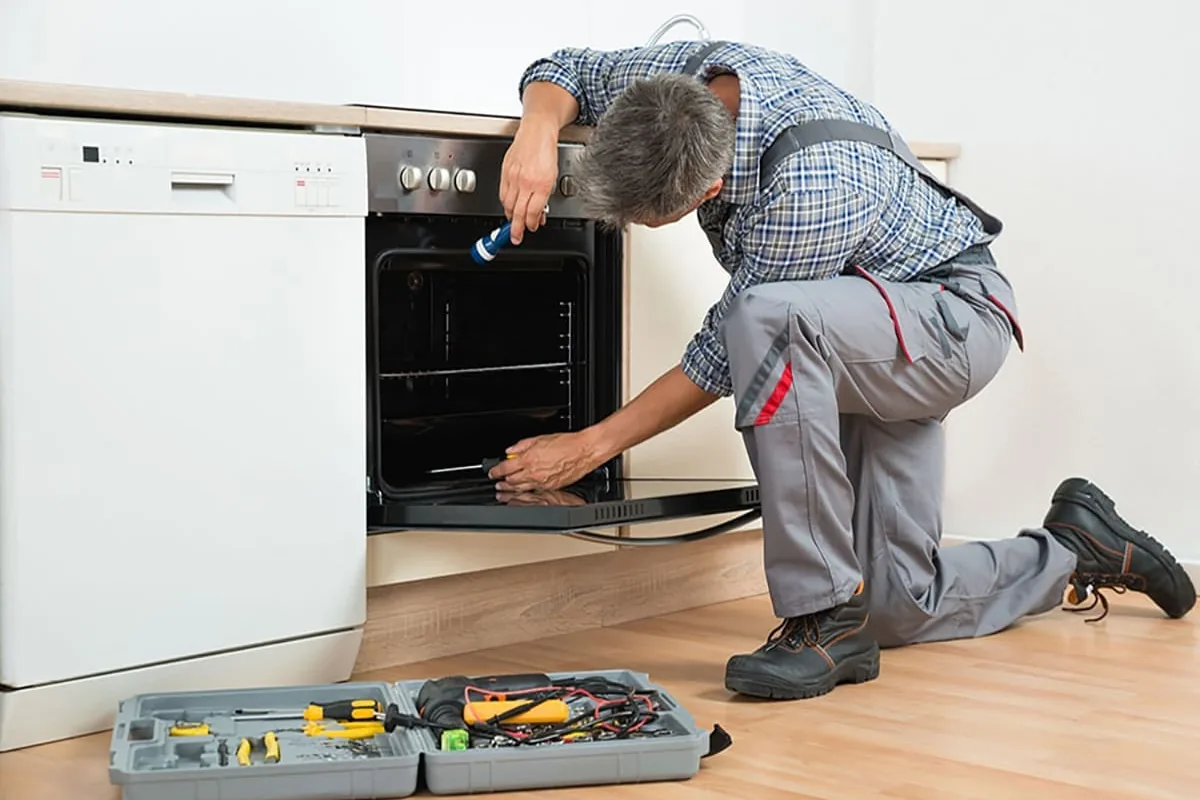 Técnico arrodillado revisando con una linterna el interior de un horno bajo encimera, junto al lavavajillas, en una vivienda de València