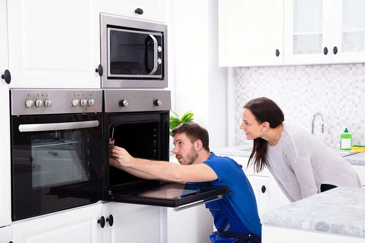 Técnico revisando con un destornillador un horno encastrado en columna, bajo el microondas, mientras la propietaria observa en una cocina de Valencia