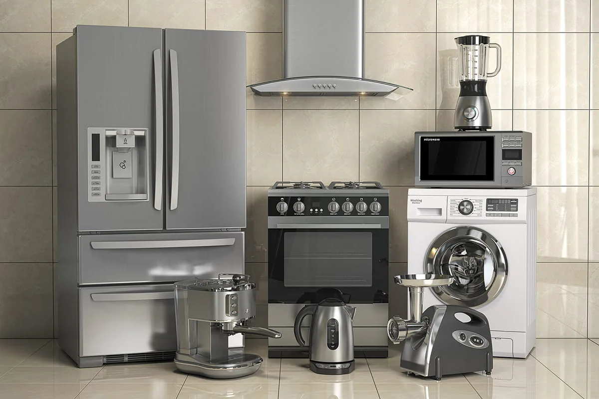 Frigorífico americano, cocina de gas con horno, campana, lavadora y pequeños electrodomésticos ante una pared de azulejo beige, como en una cocina de Elche