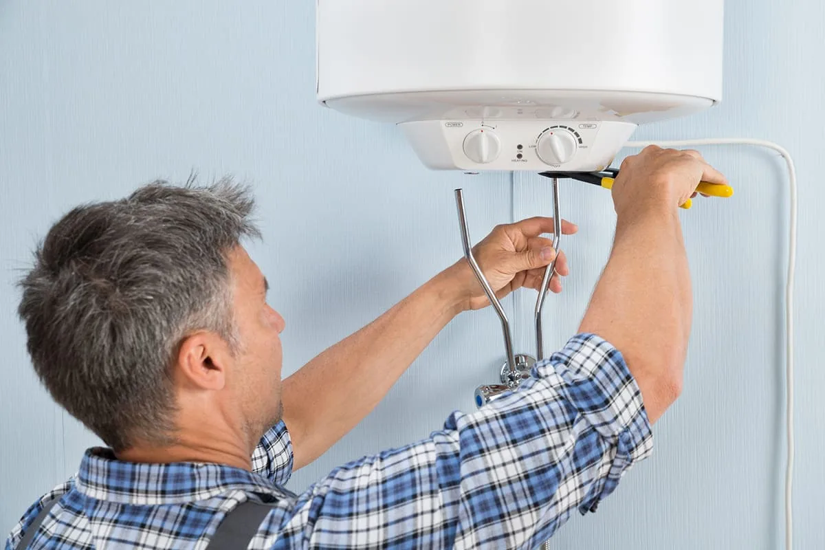 Profesional con camisa de cuadros apretando con unos alicates los tubos de entrada y salida bajo un termo eléctrico en una vivienda de A Coruña