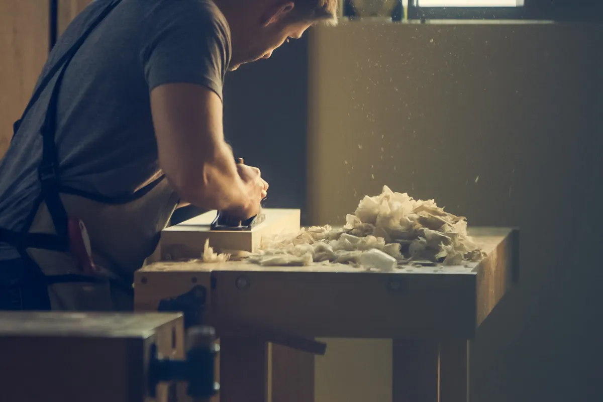 Artesano dando forma a una pieza de madera en el banco del taller entre virutas