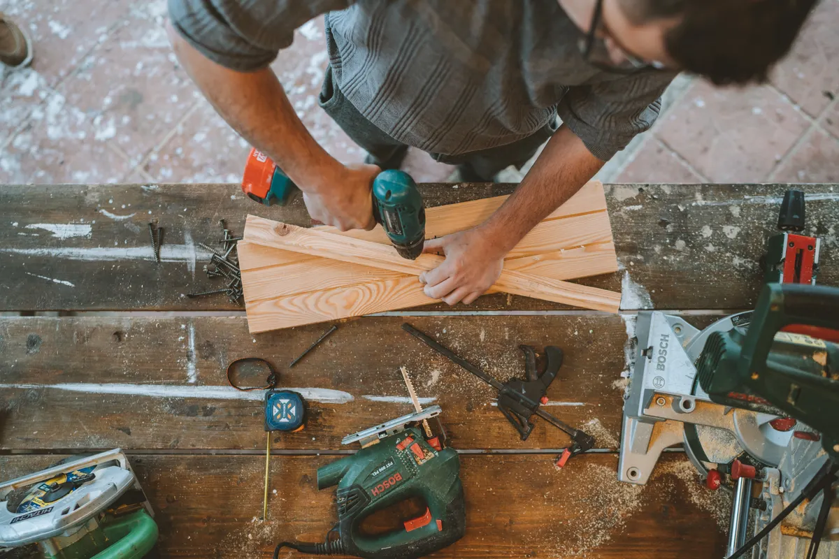 Artesano taladrando tablones de madera en un taller de carpintería rodeado de herramientas