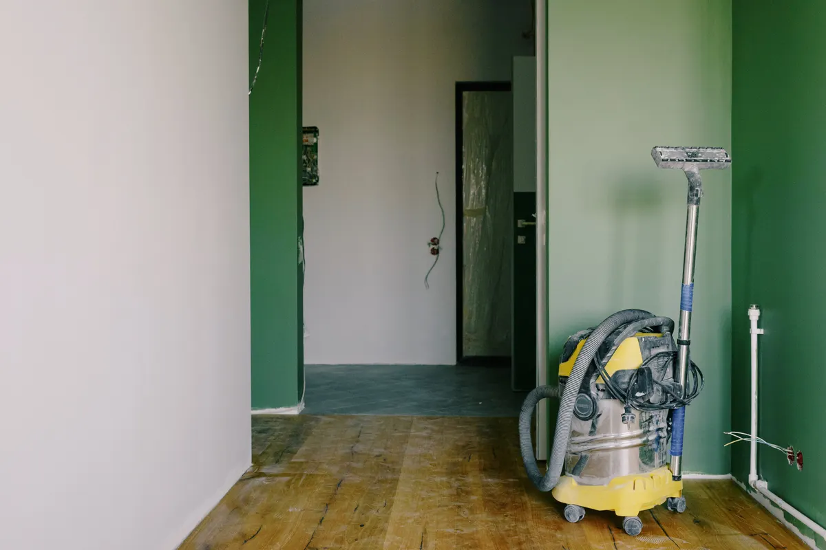 Aspiradora industrial sobre un parqué sucio en una habitación de paredes verdes durante una reforma