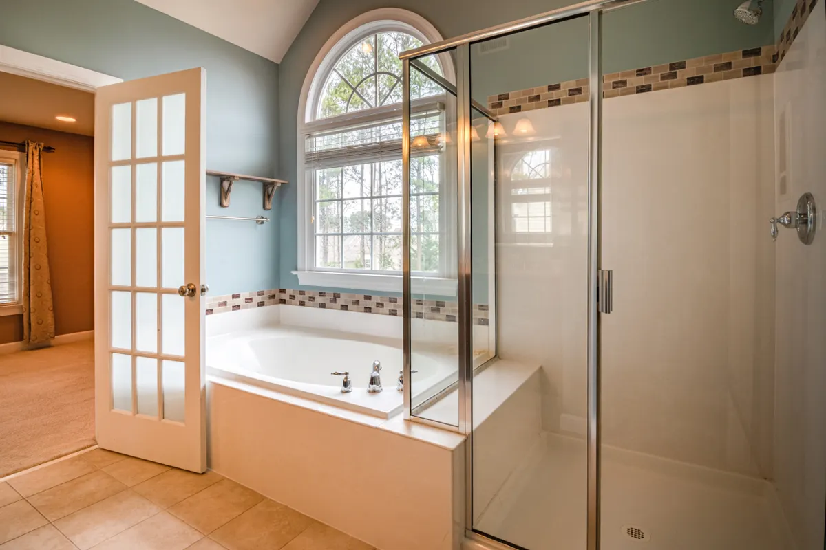 Baño amplio con ducha acristalada, bañera blanca y ventana en arco