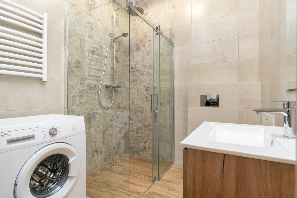 Baño con mampara de cristal, lavadora y lavabo de líneas actuales
