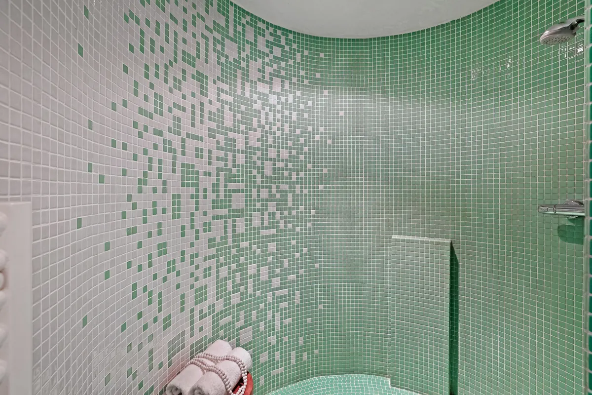 Baño pequeño con mosaico verde y blanco y toallas dobladas