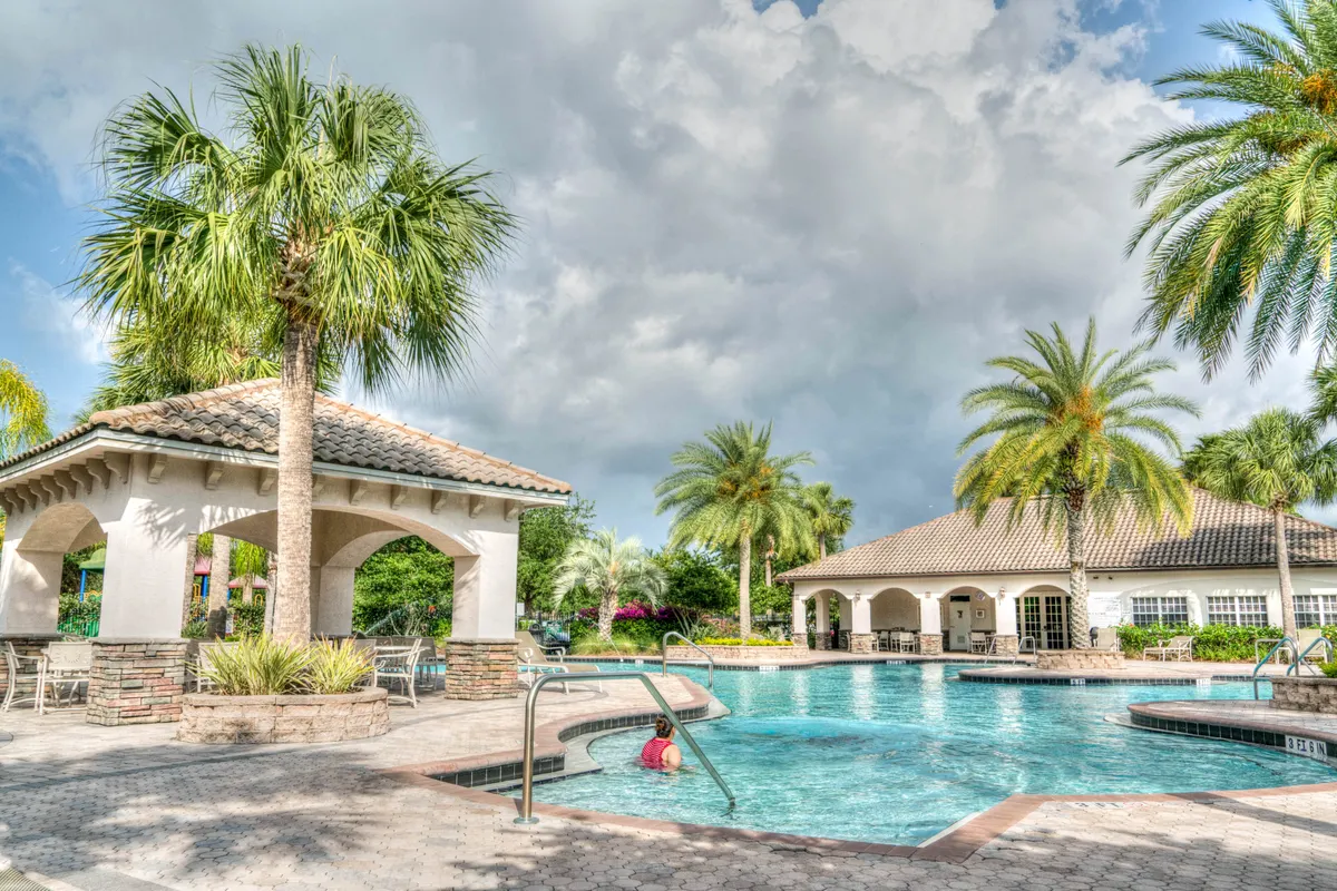 Borde de piscina con palmeras bajo un cielo con nubes