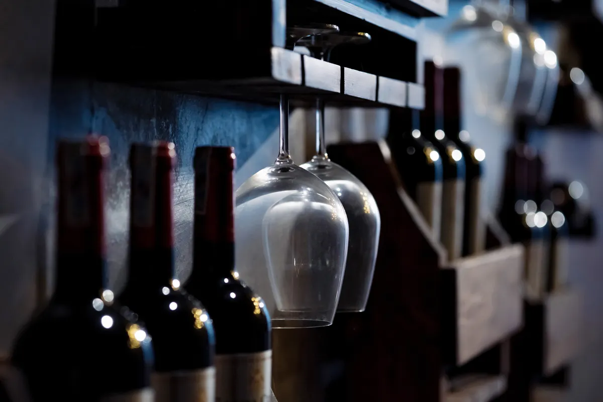 Botellas y copas de vino en estantes de madera de una bodega con poca luz