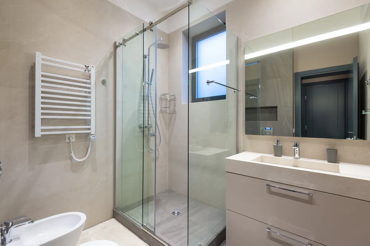 Cabina de ducha acristalada junto a un lavabo con espejo en un baño minimalista