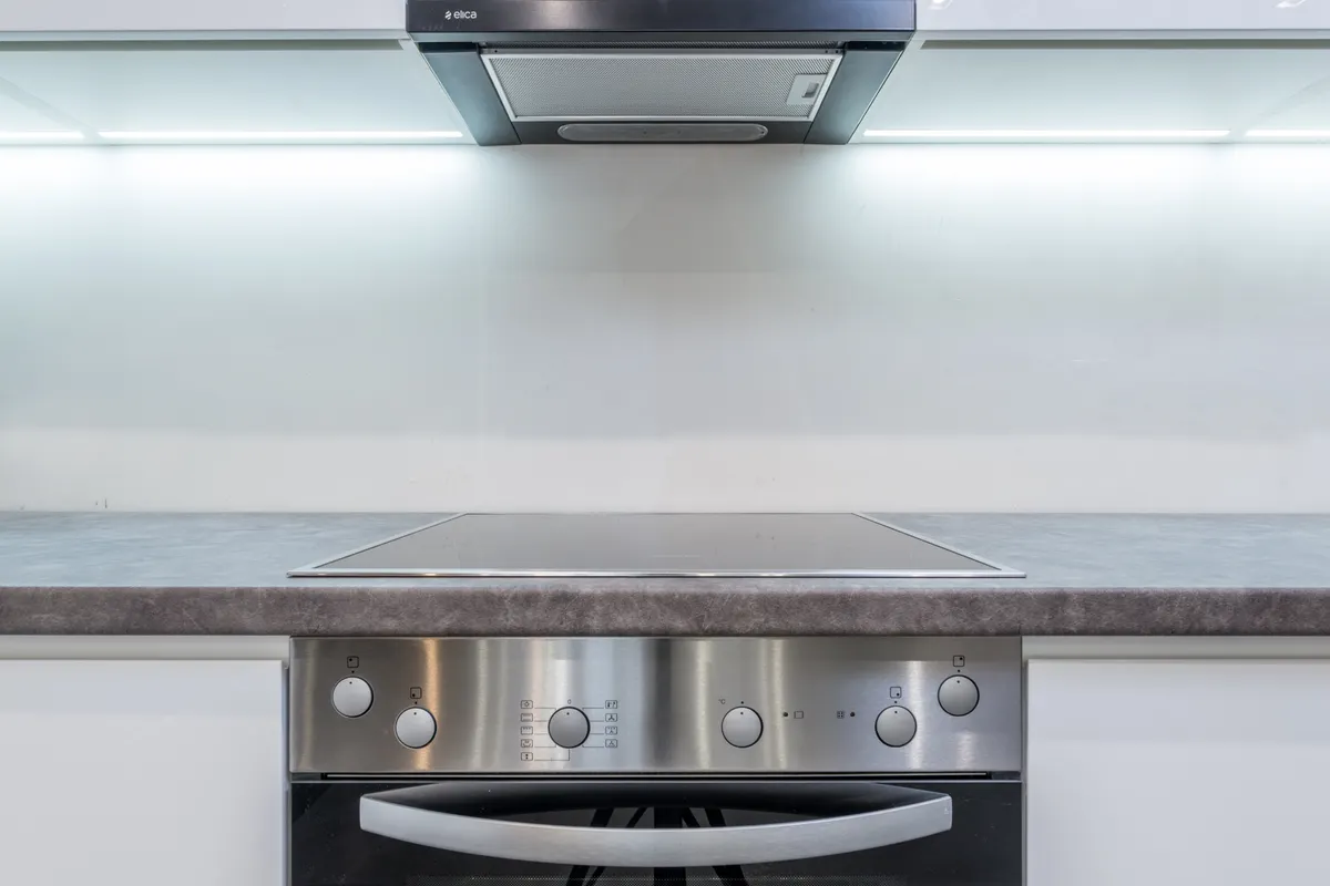 Campana extractora sobre una placa vitrocerámica y el panel de mandos de un horno empotrado en una cocina blanca