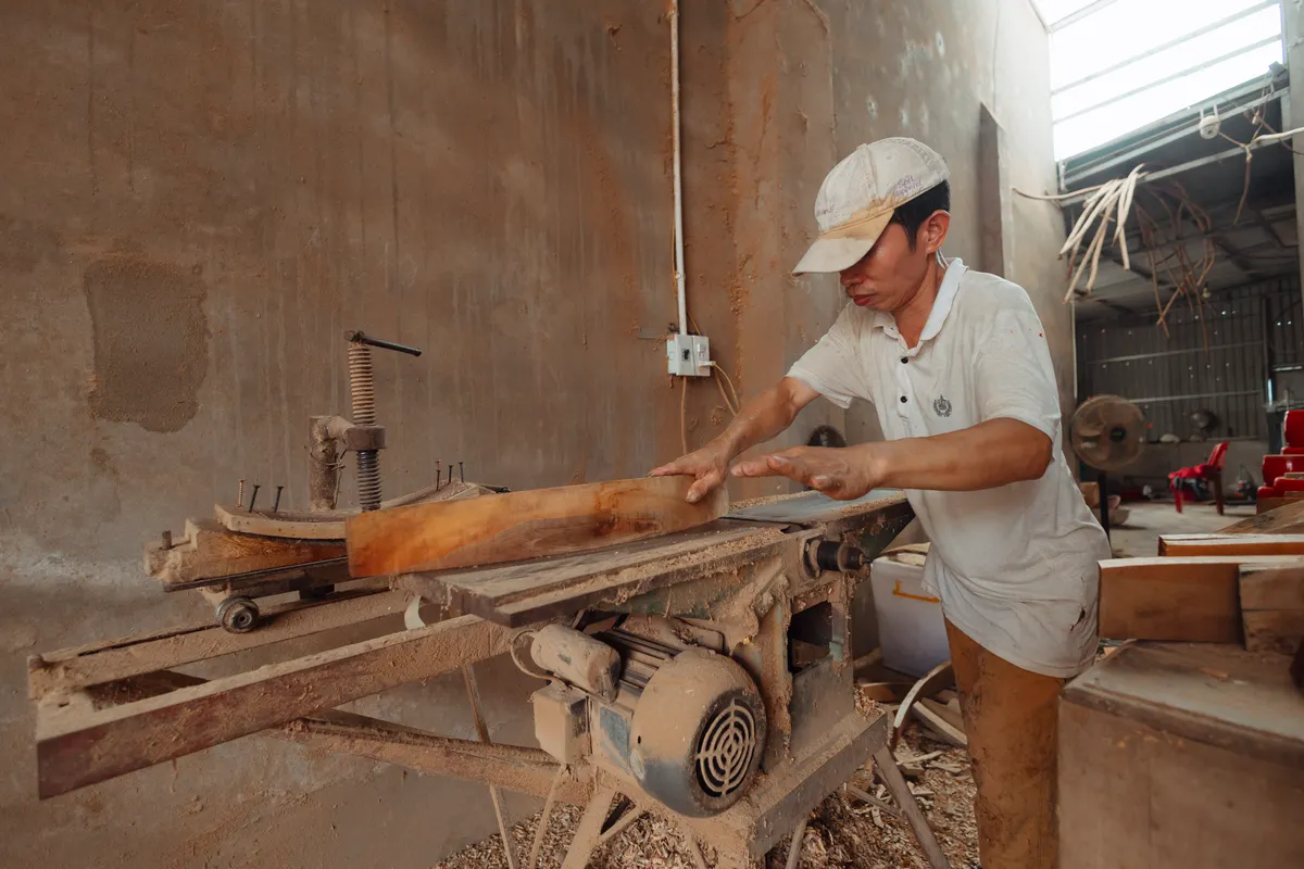 Carpintero cortando madera con una sierra industrial en un taller lleno de polvo