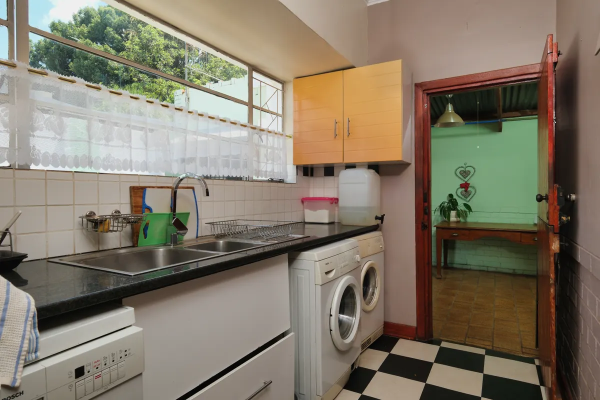Cocina estrecha con fregadero doble y una lavadora de carga frontal encajada bajo la encimera, junto a la puerta del patio