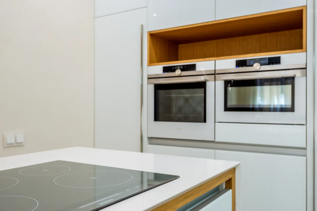 Cocina luminosa y contemporánea con hornos blancos y una placa nueva y limpia