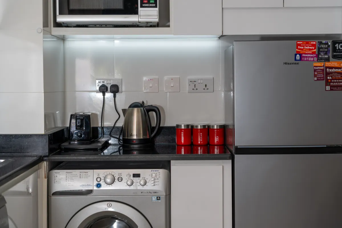 Cocina moderna con detalles rojos, lavadora, frigorífico y pequeños electrodomésticos sobre la encimera