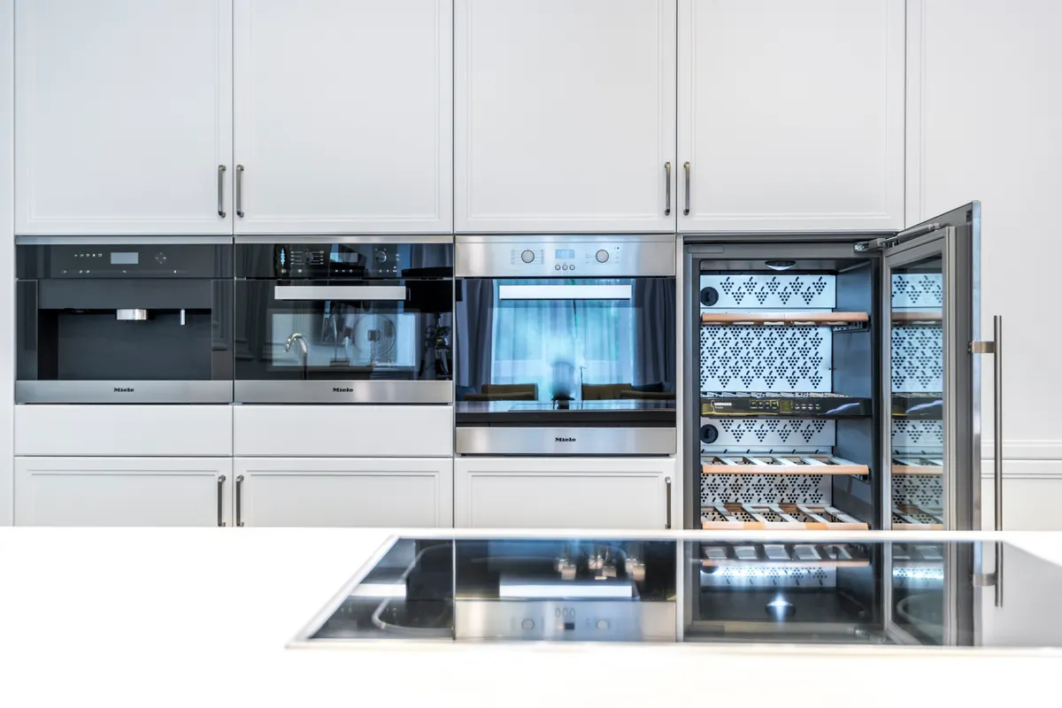 Columna de cocina con cafetera, horno y una vinoteca empotrada abierta con bandejas de madera