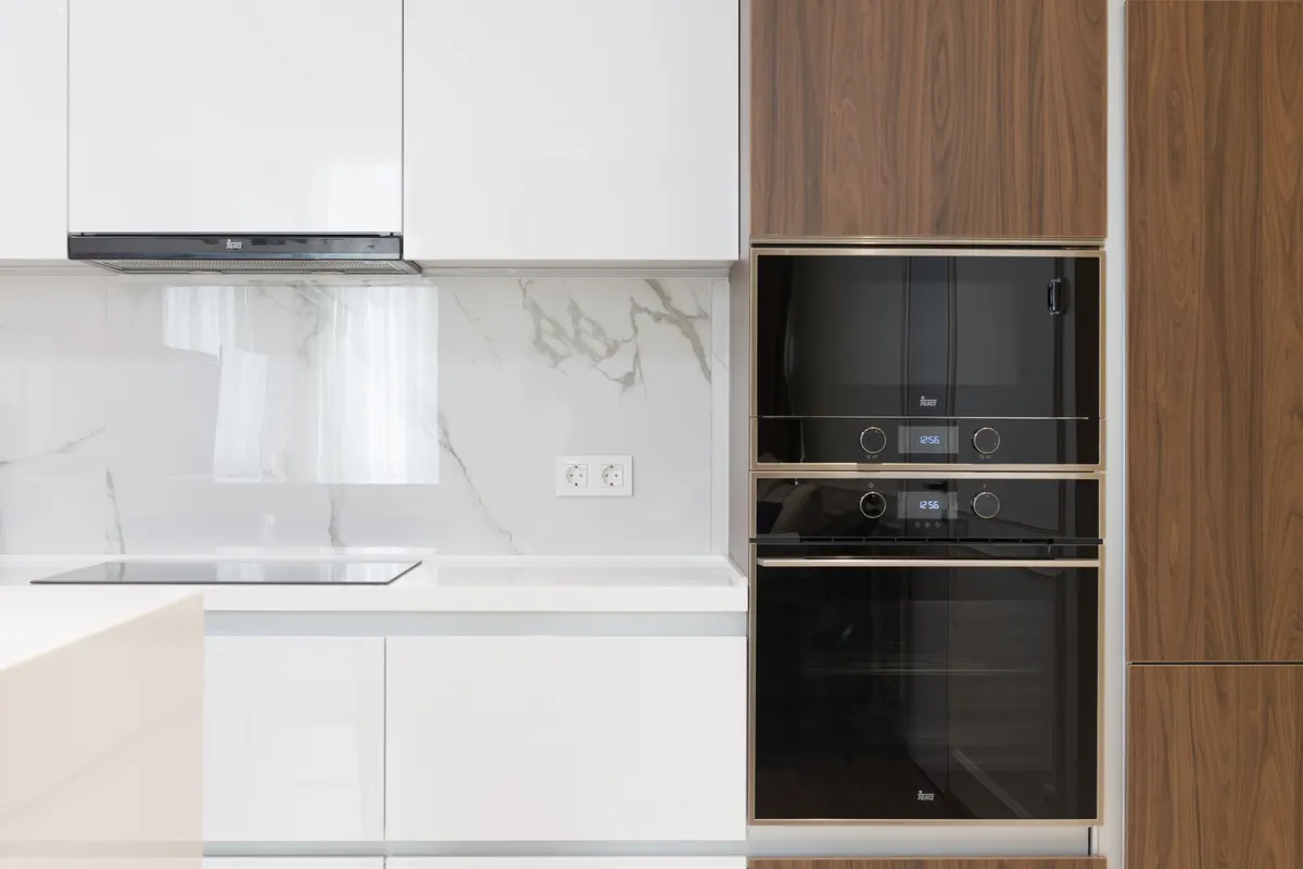 Columna de hornos empotrados en negro entre muebles blancos y de madera