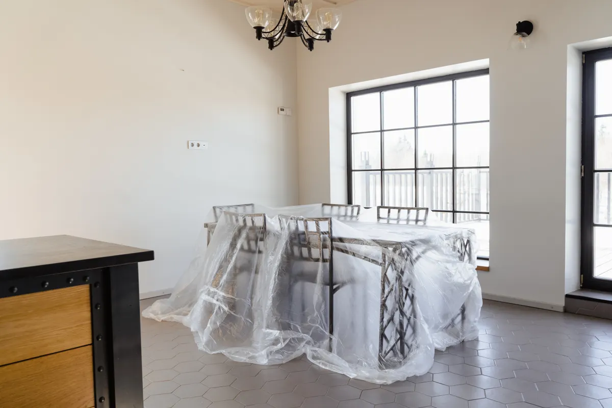 Comedor luminoso con la mesa y las sillas cubiertas con plástico protector por obras