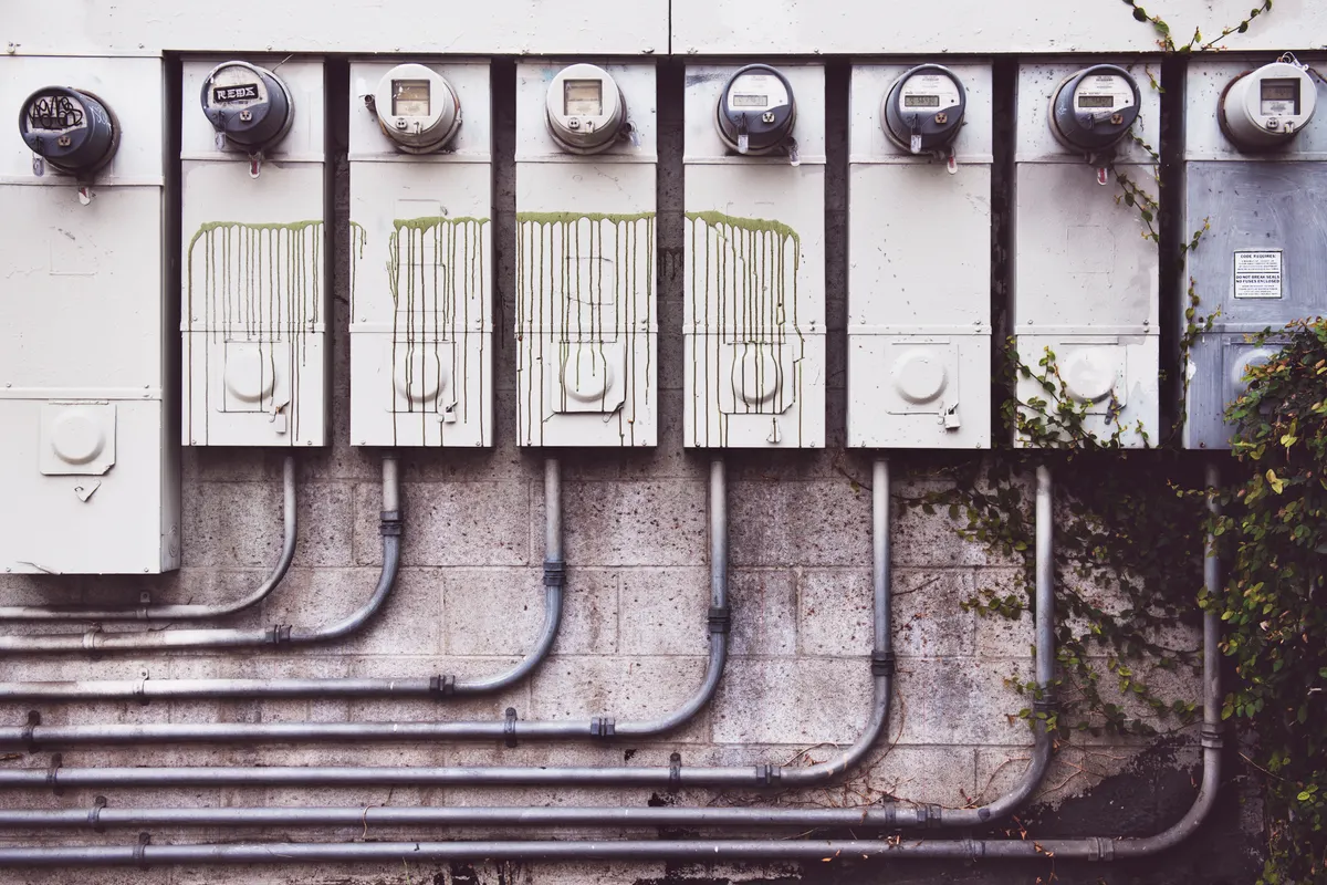 Conjunto de contadores eléctricos exteriores en una pared de ladrillo con enredaderas