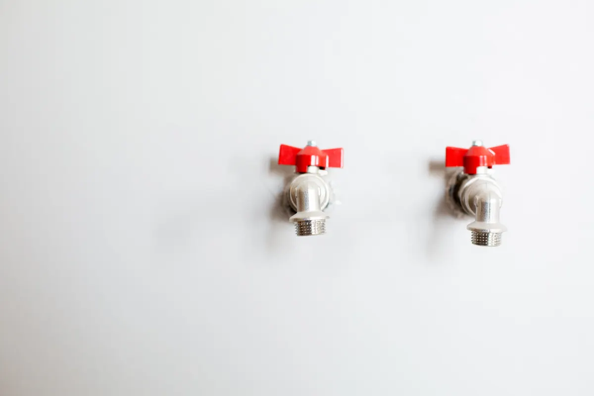 Dos llaves de paso de esfera con maneta roja y salida roscada instaladas en una pared blanca