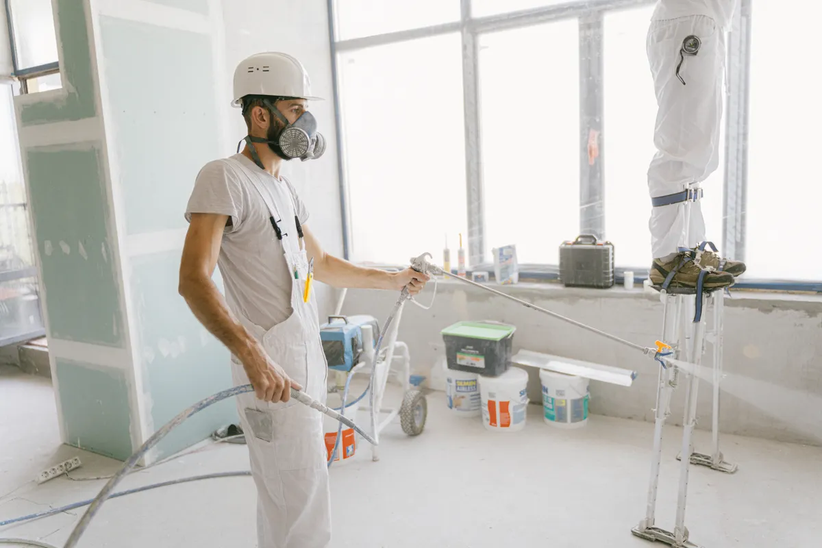 Dos operarios con equipo de protección pintando las paredes interiores en una reforma