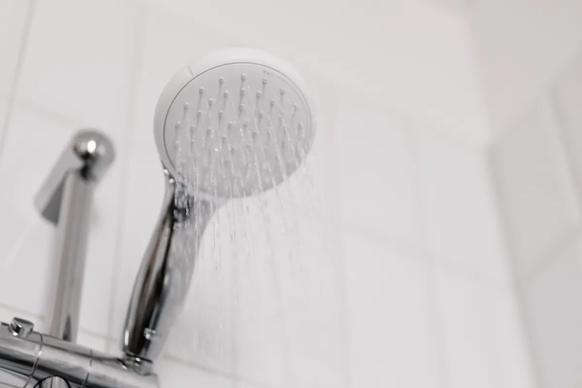 Ducha con el agua corriendo en un baño de azulejo blanco