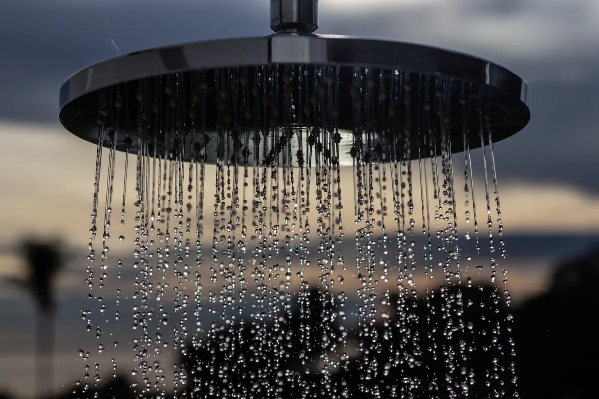 Ducha exterior con gotas de agua y un atardecer desenfocado al fondo