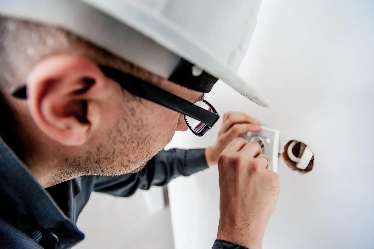 Electricista con casco y gafas montando un enchufe en la pared
