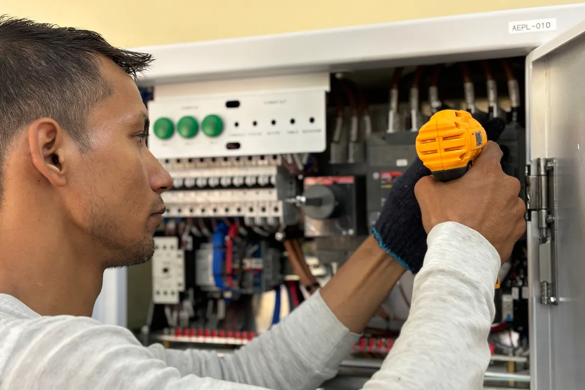 Electricista reparando un equipo eléctrico con un taladro en un espacio interior