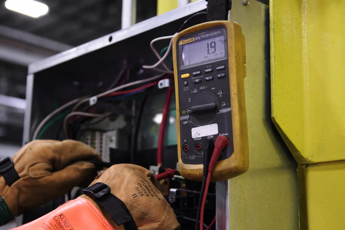 Electricista usando un multímetro para reparar el cableado de un cuadro de control industrial