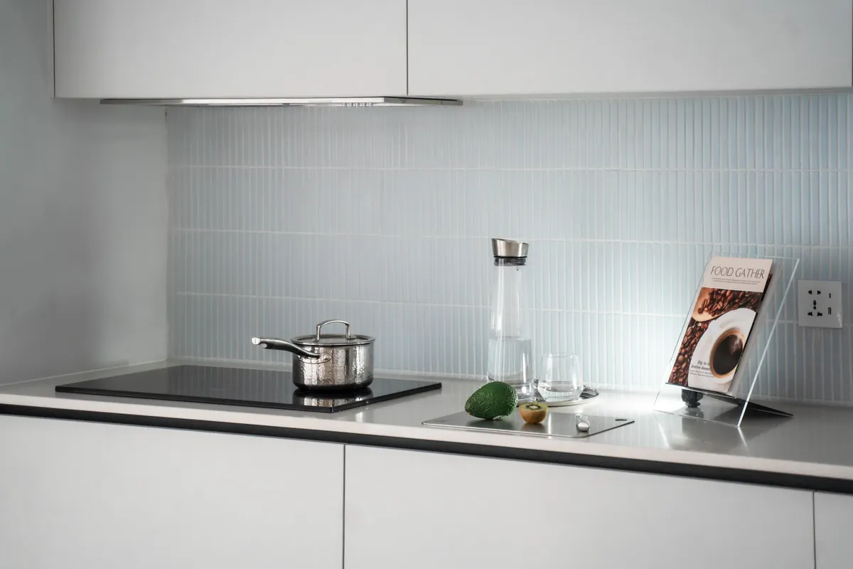 Encimera minimalista con placa de inducción, una olla, cristalería y un libro de cocina
