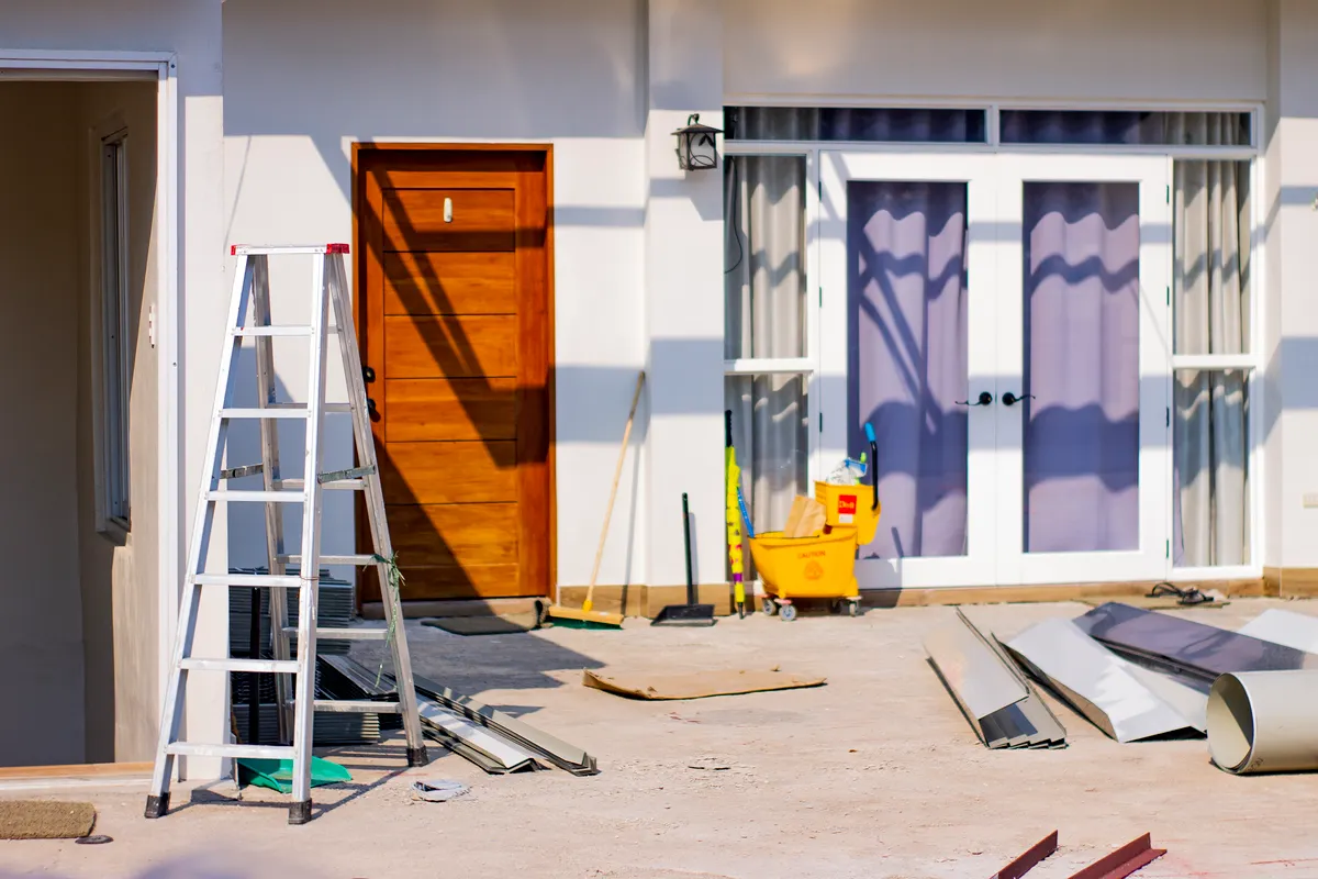 Entrada principal de una casa en obras con herramientas y materiales esparcidos