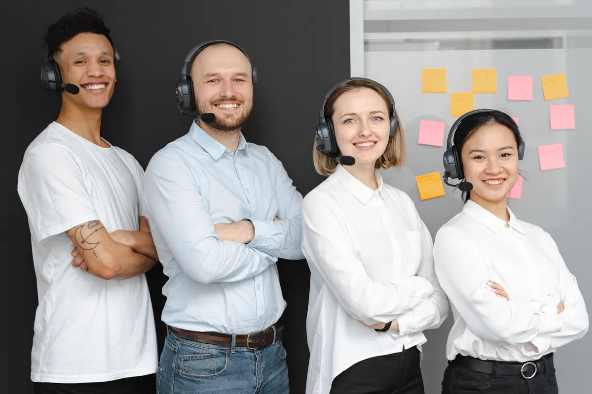 Equipo diverso de un centro de llamadas posando de pie y sonriente con auriculares y micrófonos