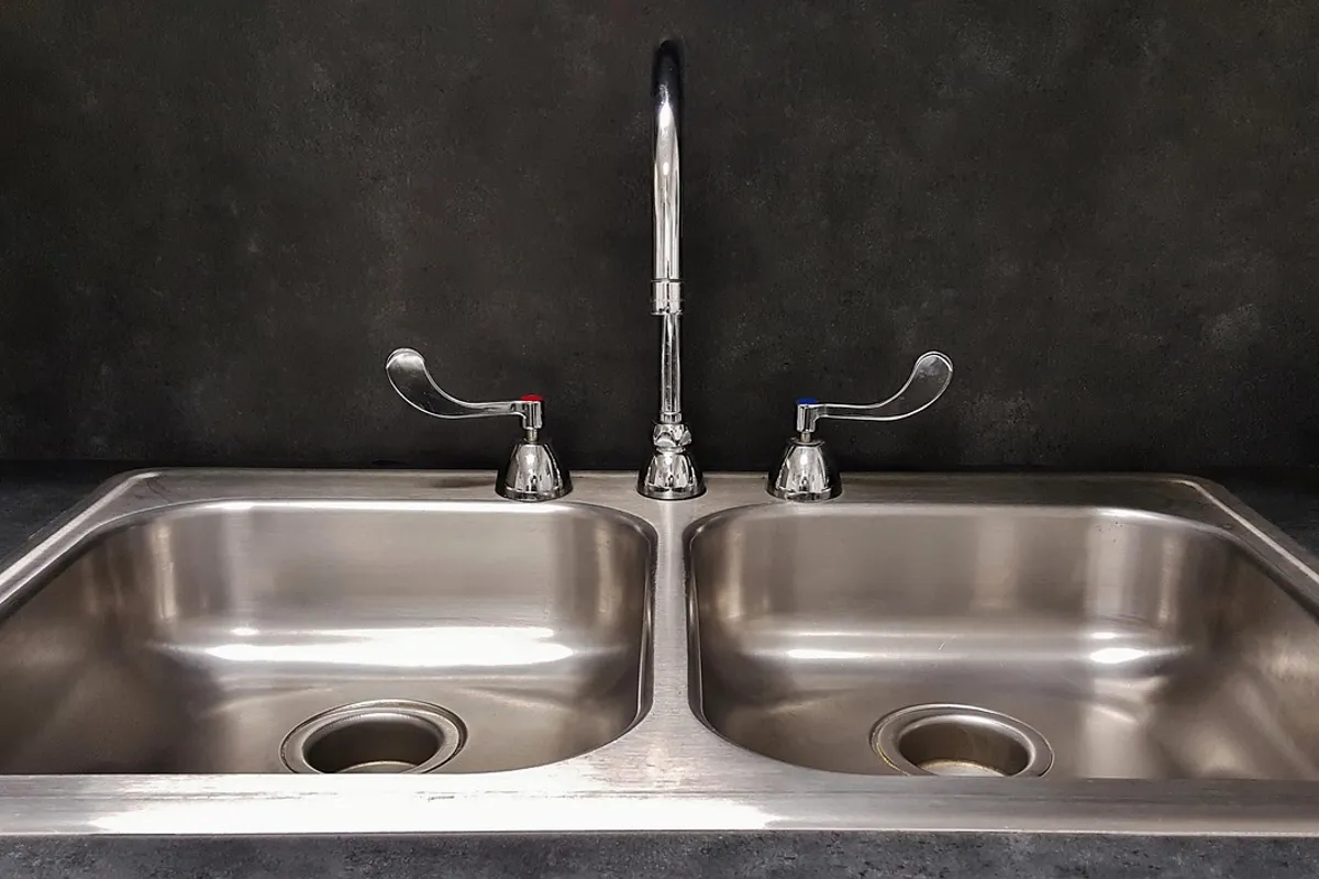 Fregadero doble de acero inoxidable con sus dos desagües y un grifo de caño alto