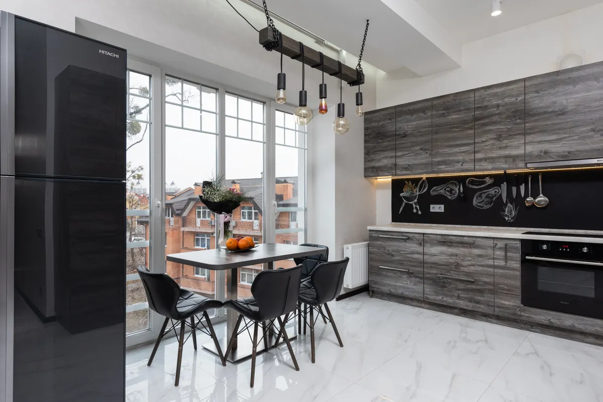 Frigorífico y mesa con sillas junto a la ventana en una cocina luminosa con armarios y menaje moderno