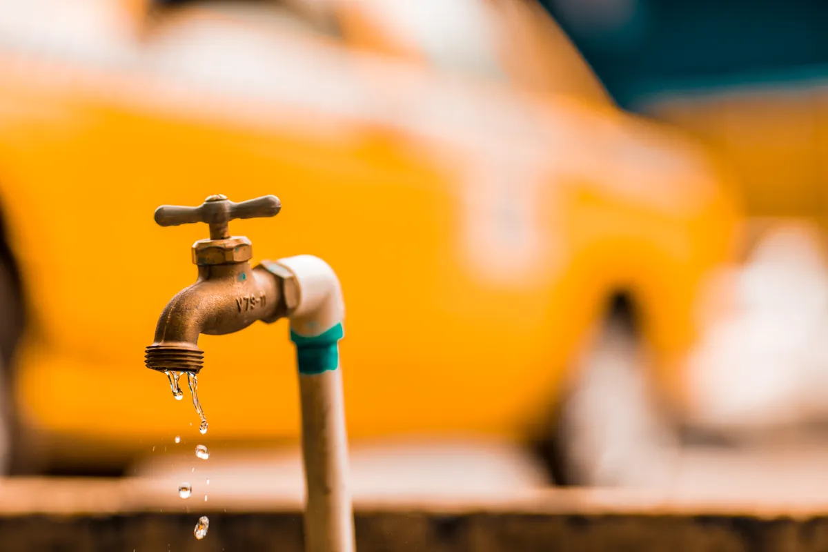 Grifo de latón con gotas de agua ante un fondo amarillo desenfocado