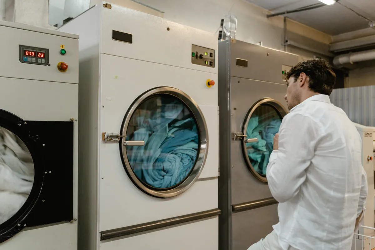 Hombre con camisa blanca usando lavadoras industriales en una lavandería pública