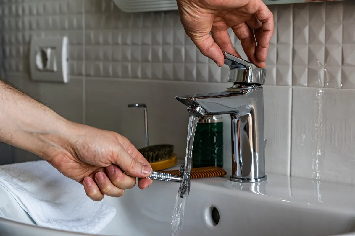Hombre enjuagando una maquinilla de afeitar bajo el grifo del baño